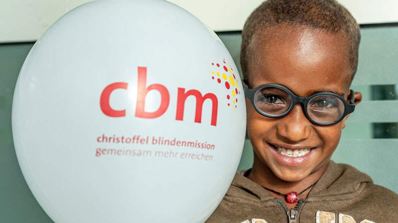 Afrikanisches Kind mit Sehbehinderung hält lachend einen CBM Luftballon